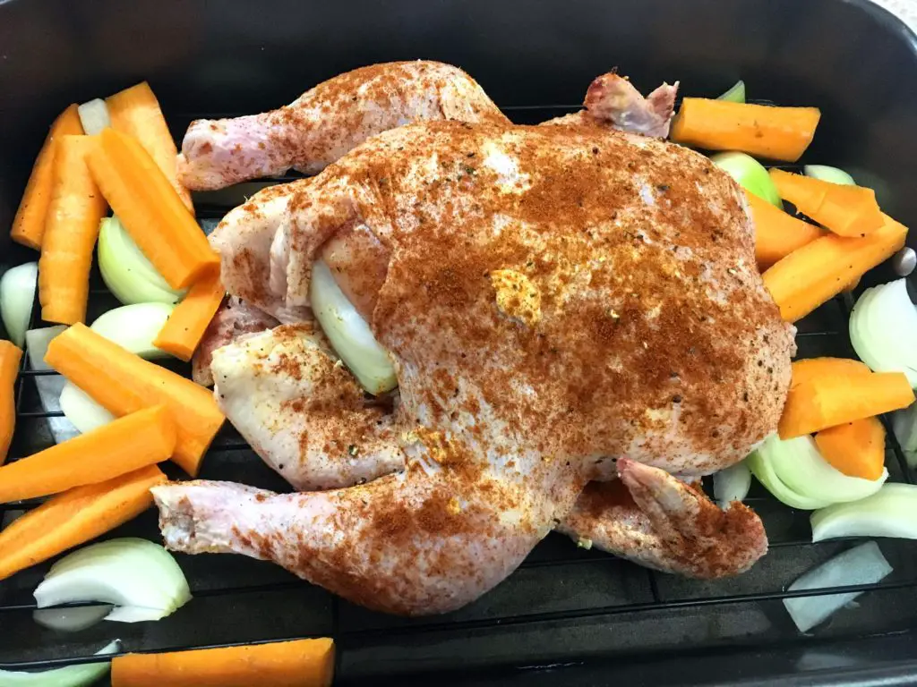 raw paprika spiced chicken in roasting pan with carrots and onions