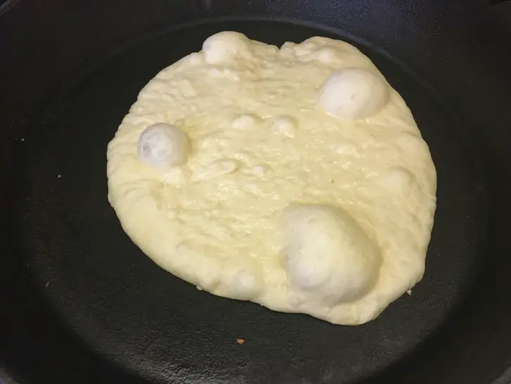 bubbly naan in a cast iron skillet