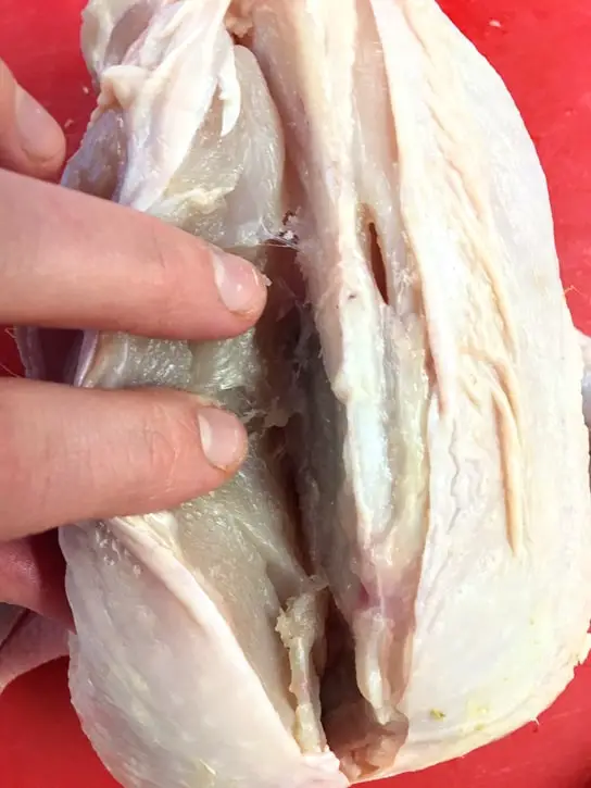cutting into a chicken to remove the breasts